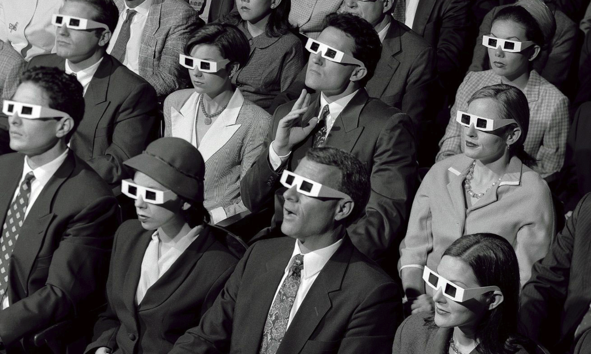 A black and white photo of movie goers dressed in formal wear and wearing paper 3D glasses.